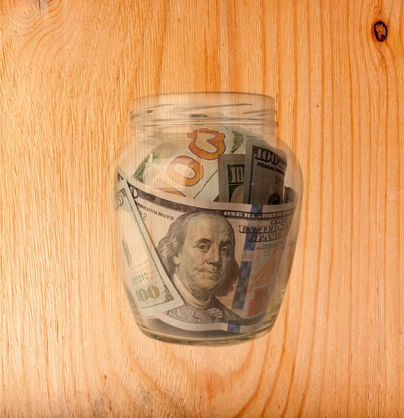Cent dollars billets dans un bocal en verre isolé sur fond de bois — Photo