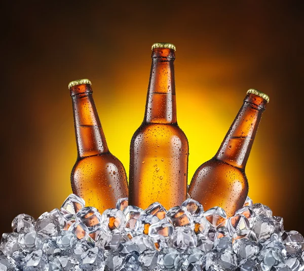 Três garrafas de cerveja nos cubos de gelo no fundo amarelo . — Fotografia de Stock