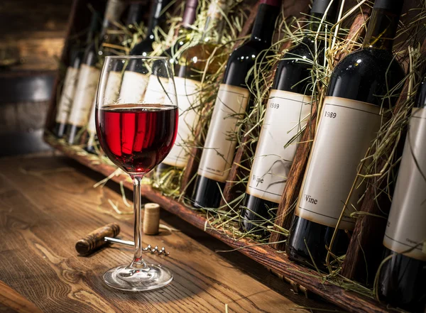 Glas Rotwein und Weinflaschen auf dem Hintergrund. — Stockfoto