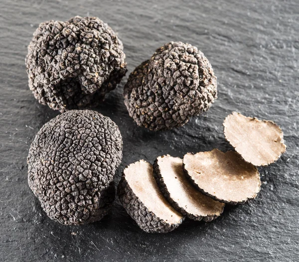 Black truffles and truffle slices on the graphite board. — Stock Photo, Image