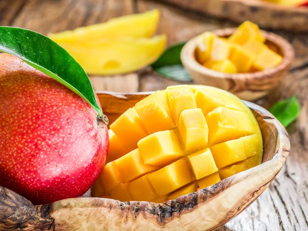 Owoce mango i pokrojone w kostkę mango na drewnianym stole. — Zdjęcie stockowe