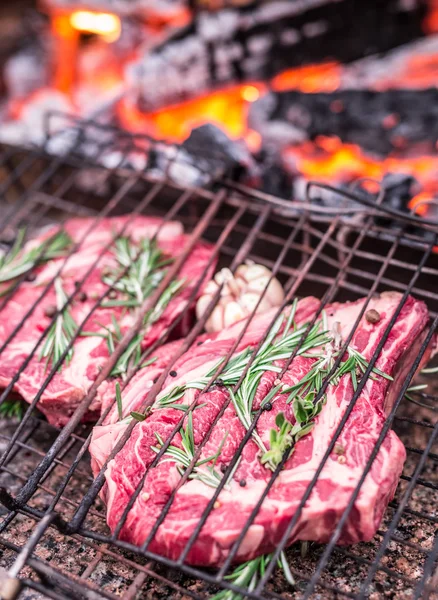 Rib eye steaks and grill with burning fire behind them. — Stock Photo, Image