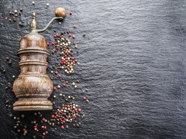 Colorful peppercorns and old pepper mill on the black background — Stock Photo, Image