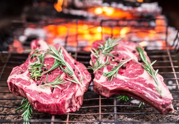 Rib Eye Steaks und Grill mit loderndem Feuer dahinter. — Stockfoto