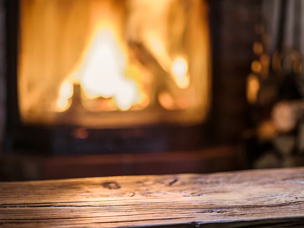 Old wooden table and fireplace with warm fire on the background. — Stock Photo, Image