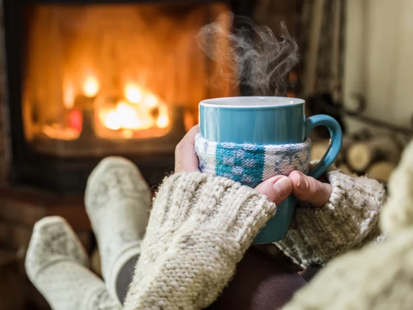 Calentamiento y relajación cerca de la chimenea con una taza de bebida caliente . — Foto de Stock