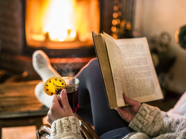 Hot mulled wine and book in woman hands. Relaxing in front of bu