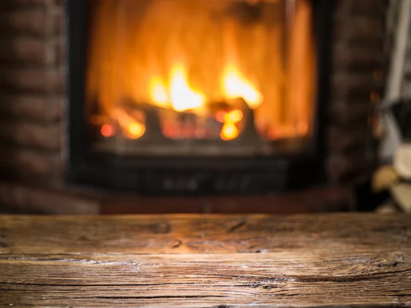Alter Holztisch und Kamin mit warmem Feuer im Hintergrund. — Stockfoto