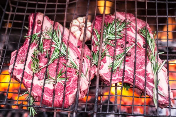 Rib Eye Steaks und Grill mit loderndem Feuer dahinter. — Stockfoto