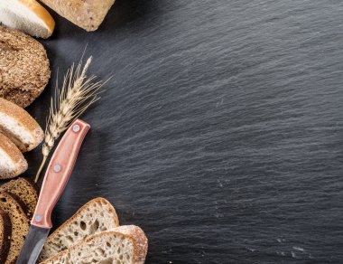 Ekmek dilimleri, bir buğday ve siyah taş masa üzerinde bir bıçak.