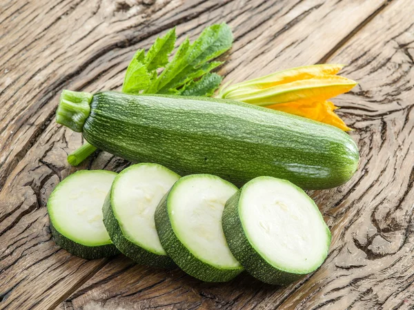 Courgette met segmenten en courgette bloemen op een houten tafel. — Stockfoto