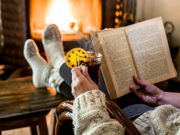 Hot mulled wine and book in woman hands. Relaxing in front of bu