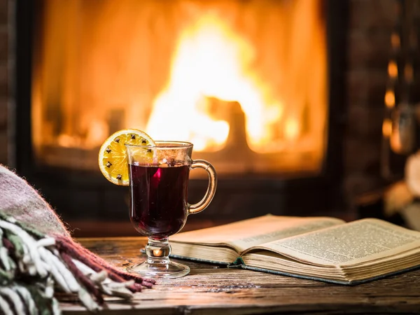 Hot mulled wine and a book on the wooden table. Fireplace with w — Stock Photo, Image