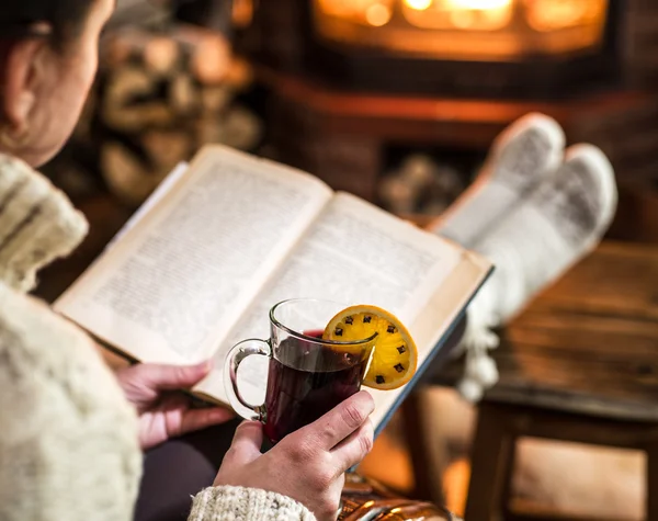 Vinho quente quente e livro em mãos de mulher. Relaxando na frente do bu — Fotografia de Stock