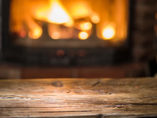 Alter Holztisch und Kamin mit warmem Feuer im Hintergrund. — Stockfoto