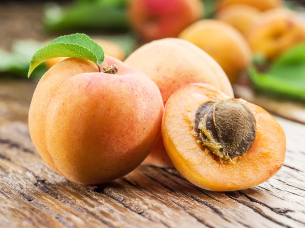 Apricots and its cross-section on the old wooden table. — Stock Photo, Image