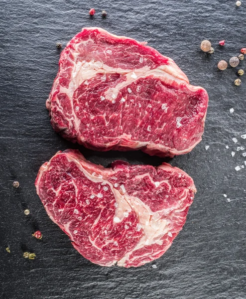 Rib eye steaks with spices on the black background. — Stock Photo, Image