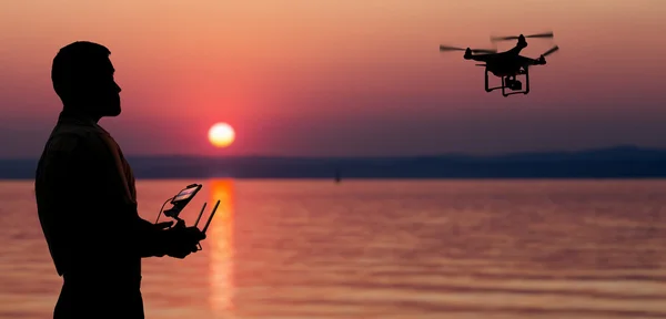 Mann fliegt bei Sonnenuntergang mit Drohne am Meer. — Stockfoto