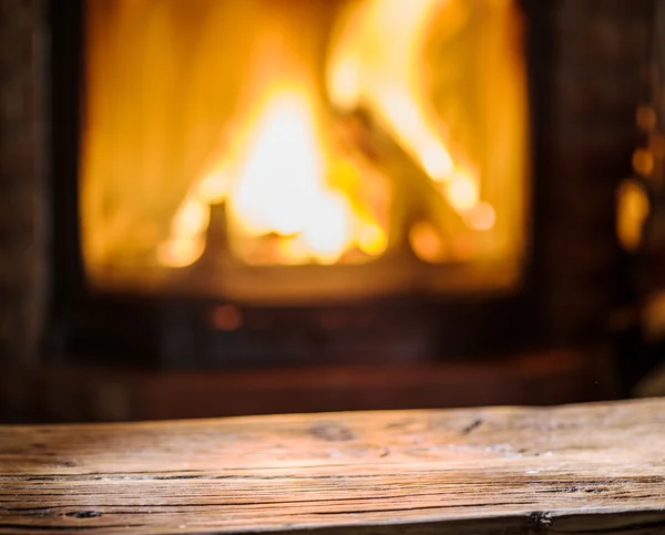 Starý dřevěný stůl a krb s ohni na pozadí. — Stock fotografie