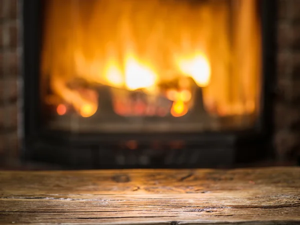 Alter Holztisch und Kamin mit warmem Feuer im Hintergrund. — Stockfoto