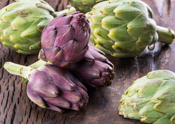 Green and purple artichoke flower edible buds on wooden background.