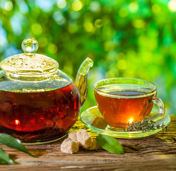 Tea ceremony. Glass teapot with brewed tea is on the table on a sunny summer day. In the background bokeh of beautiful nature.