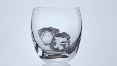 Buz küpleri bardağa düşer ve sonra viski dökülür. Beyaz arkaplanda nesne.