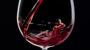 Kırmızı şarap siyah arka plandaki bir bardağa dökülüyor. Yakın çekim.