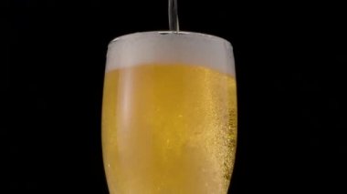 Siyah arka planda bir bardak light bira. Bir jet kadehi yavaşça bira ile doldurarak bol köpük ve kabarcıklara neden olur. Saat yönünde döndürme.