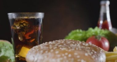 Kamera fast food yemek masasında yavaşça hareket ediyor. Kola ve patates kızartması, sulu bir hamburgerin önünde duruyor. Blackmagic Cep Sineması Kamera 6K.