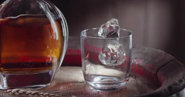 冰块慢慢地落在威士忌桶上的威士忌杯中 旁边站着一个酒壶 背景是深褐色的 黑魔法Ursa Pro — 图库视频影像