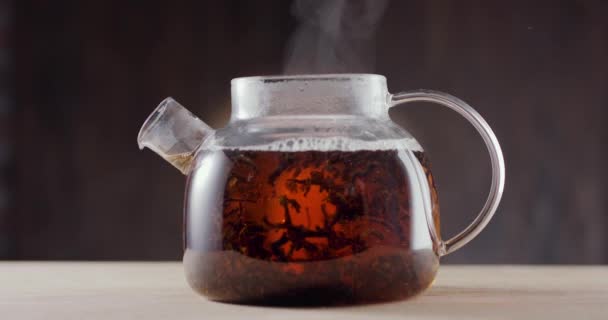 在一个装有开水和大叶茶的杯子茶壶里 煮好的红茶叶子慢慢地旋转着 深褐色背景 慢动作150 Fps 黑魔法Ursa Pro — 图库视频影像