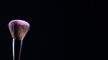 Makyaj fırçası titrer ve ince pembe toz parçacıkları oluşturur. Siyah arka plan, yavaş çekim, 300 fps.