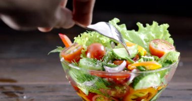 Elinde çatal dikenli bir el cam kaseden taze bir sebze salatası, siyah bir arka planda..  