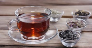 Damla yavaşça bir bardak çaya düşer. Etrafta farklı yaprak çayları olan küçük kaseler var. Klasik ahşap masa.. 