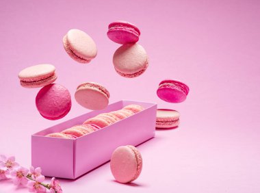Renkli tatlı badem kurabiyeleri, karton kutunun üstünde havada uçuşan aromalı kurabiyeler..