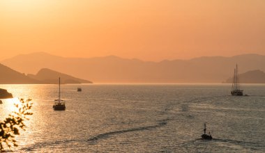 Sakin deniz ve gün batımı. Güneş ufuktaki tepelerin ardında batıyor. Güzel doğa arkaplanı.