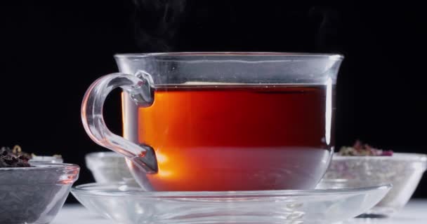 ゆっくりと黒の背景に熱いお茶のガラスカップに落ち 蒸気が上昇 — ストック動画