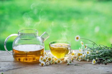 Çaydanlık ve çay bardağının yanında papatya çayı ve papatya çiçeği. Kırsal ya da kırsal arkaplan.