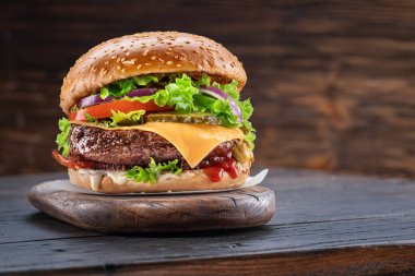 Arkası koyu kahverengi olan ahşap bir masada lezzetli bir hamburger. Fast food konsepti.