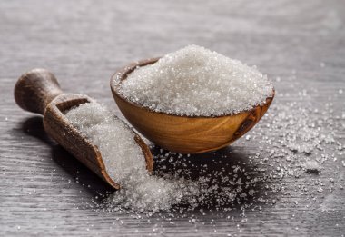 Tahta kasede beyaz rafine şeker ve koyu ahşap masada kaşık. 