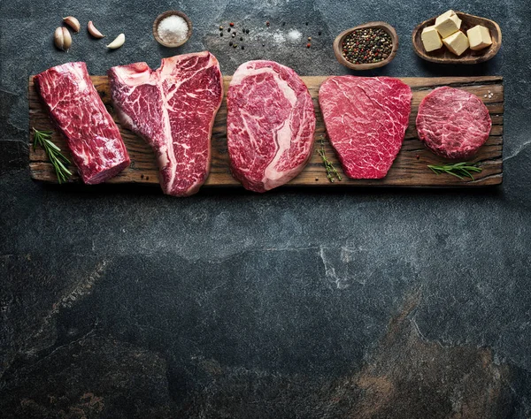 stock image Different raw beef steaks on the wooden board on the grey table. Top view.