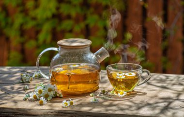 Çaydanlık ve çay bardağının yanında papatya çayı ve papatya çiçeği. Kırsal ya da kırsal arkaplan.