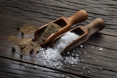 Tahta kaşıklarda eski ahşap arka planda deniz tuzu ve karabiberi. Yiyeceğe kattığın en popüler iki malzeme..  