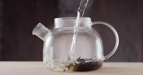 将沸腾的水倒入一个玻璃杯茶壶中 茶壶里装着大叶茶 深褐色背景 慢动作150 Fps 黑魔法Ursa Pro — 图库视频影像