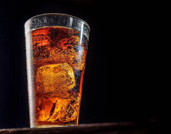 Chilled glass of cola drink with ice cubes isolated on dark background.