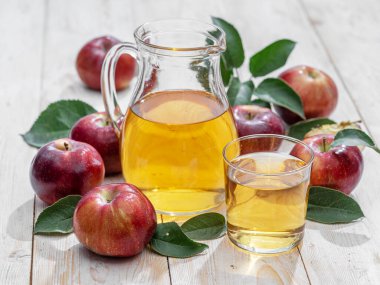 Bir bardak meyve suyu, bir sürahi taze elma suyu ve ahşap masada organik elmalar..