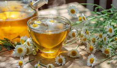 Tahta masada bir bardak papatya çayı ve papatya çiçeği. Yakın plan..