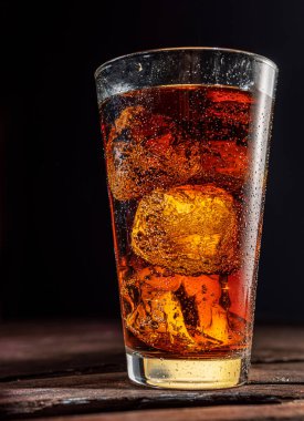 Koyu arkaplanda buz küpleri olan soğuk bir bardak kola..