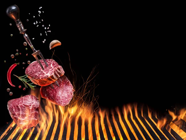 Grilled beef steaks in motion falling down on open grill. Conceptual photo of meat or barbeque cooking process.